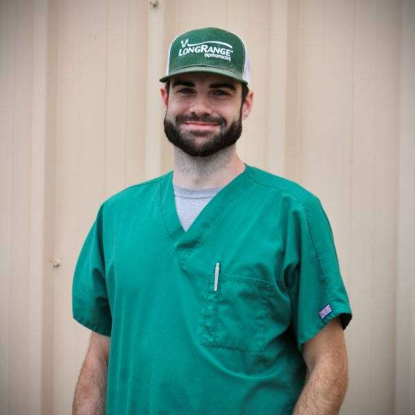 A man in green scrubs and a green cap stands smiling.