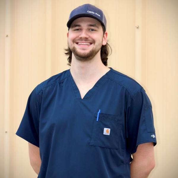 Person wearing a navy scrub top and cap, smiling with hands behind back against a neutral background.