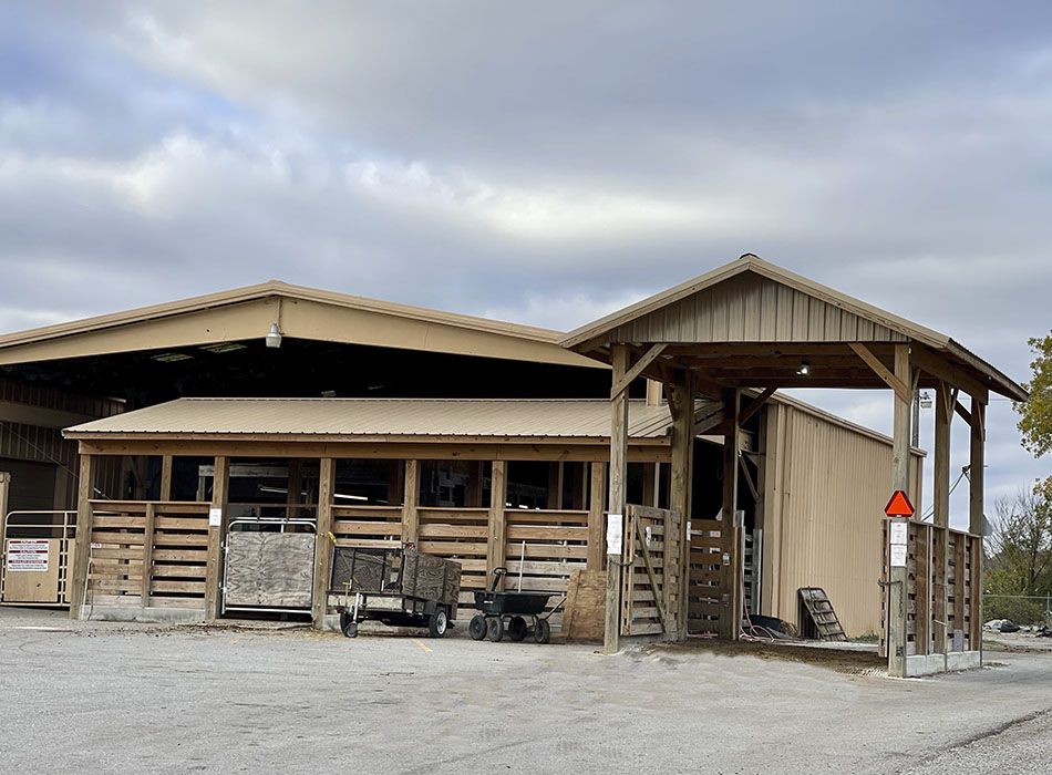 A covered wooden building with open sections, wagons, and a gravel lot under a cloudy sky.