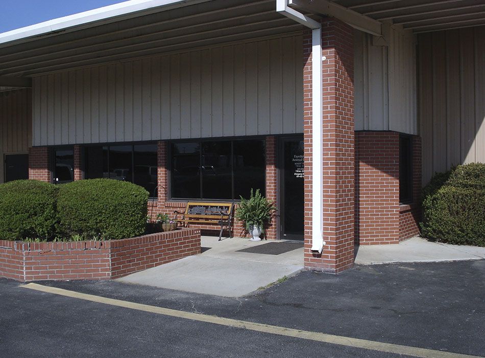Brick building entrance with a canopy, bushes, and a bench next to the door.