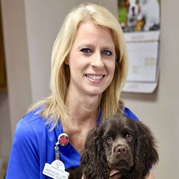 A smiling woman in a blue uniform holding a small brown dog.