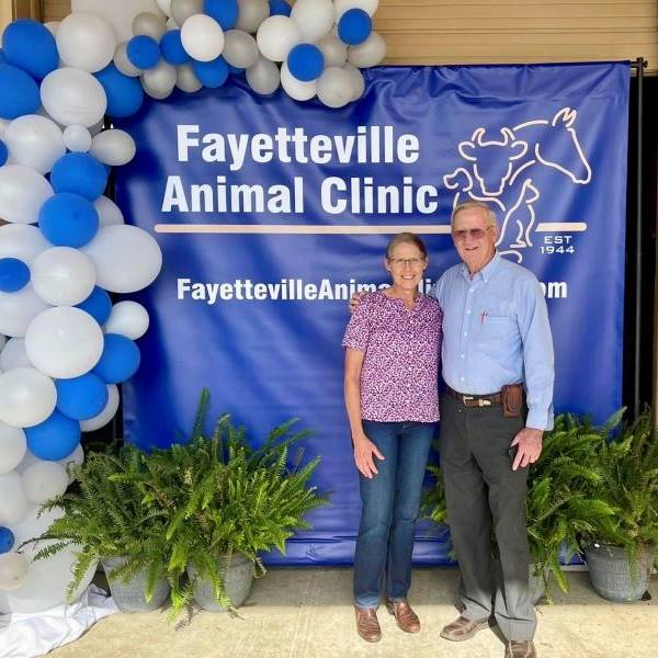 Two people standing in front of a backdrop with "Fayetteville Animal Clinic" and balloon decorations.